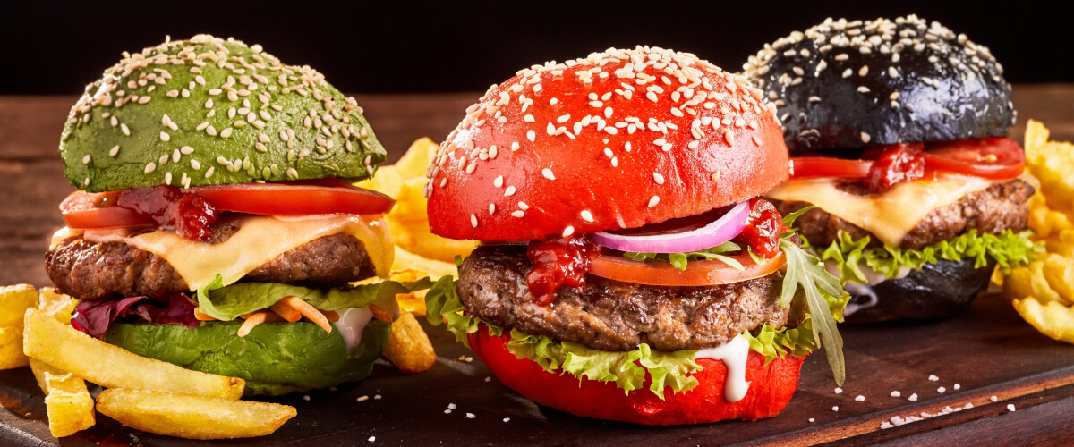 Beef Burger mit bunten Burgerbrötchen in Rot, Schwarz und Grün und Pommes auf Holztablett