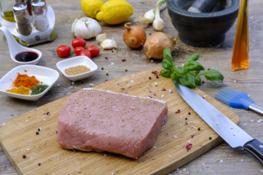 Ein Stück Schweinefleisch auf Holzbrett mit Messer, Rub und Marinade